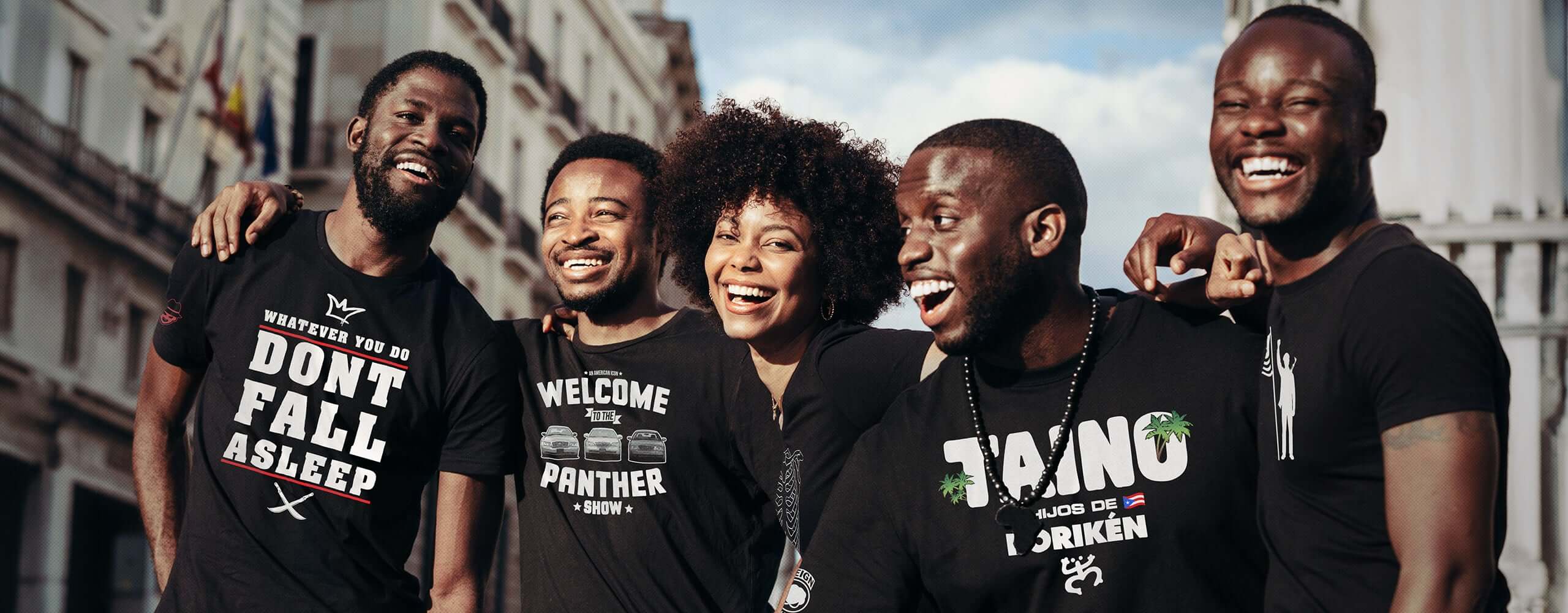 Five people wearing black t-shirts with various text, standing together outdoors.